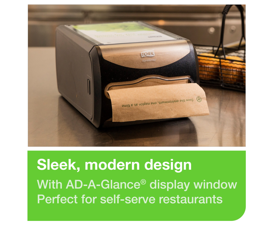 A black napkin dispenser with a brown paper napkin on a stainless steel countertop near a wire basket. Tork Xpressnap® Counter Napkin Dispenser (7.5 in. x 5.7 in. x 12.1 in., 1/Case)